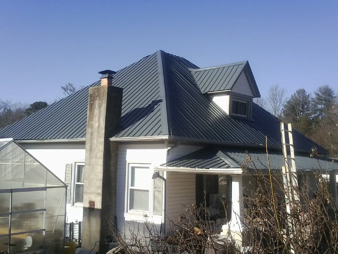 Dark blue standing seam metal roof on a white farmhouse with dormer — Slate & Tile Roof Repair by Roofing Brothers in Moundridge