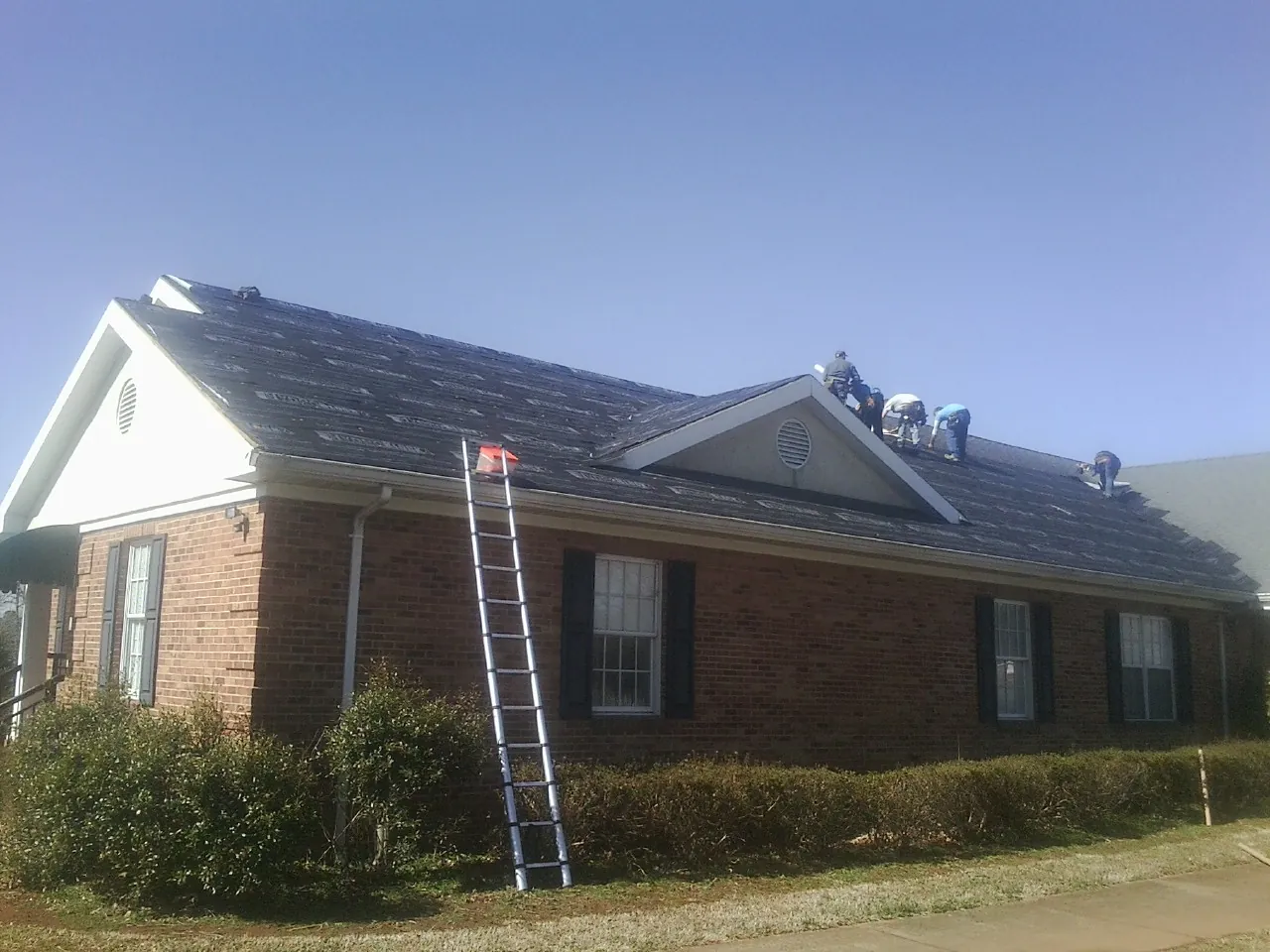 Crew tearing shingles off a brick ranch roof with a ladder set — Emergency Roof Repair work by our crew in Moundridge