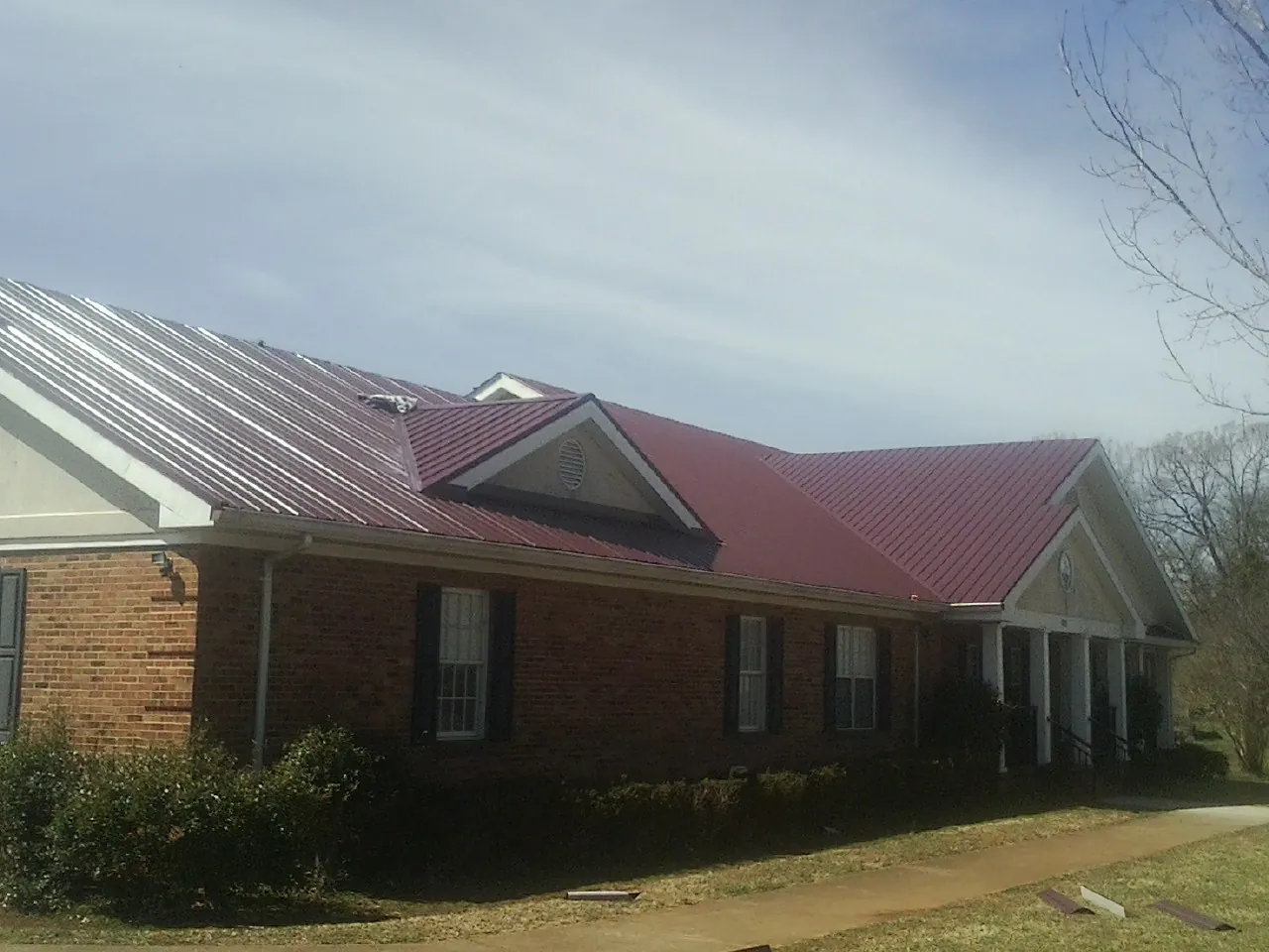 Red metal roof with gabled entries on a long brick building, from a Hail Damage Roof Repair job in Moundridge