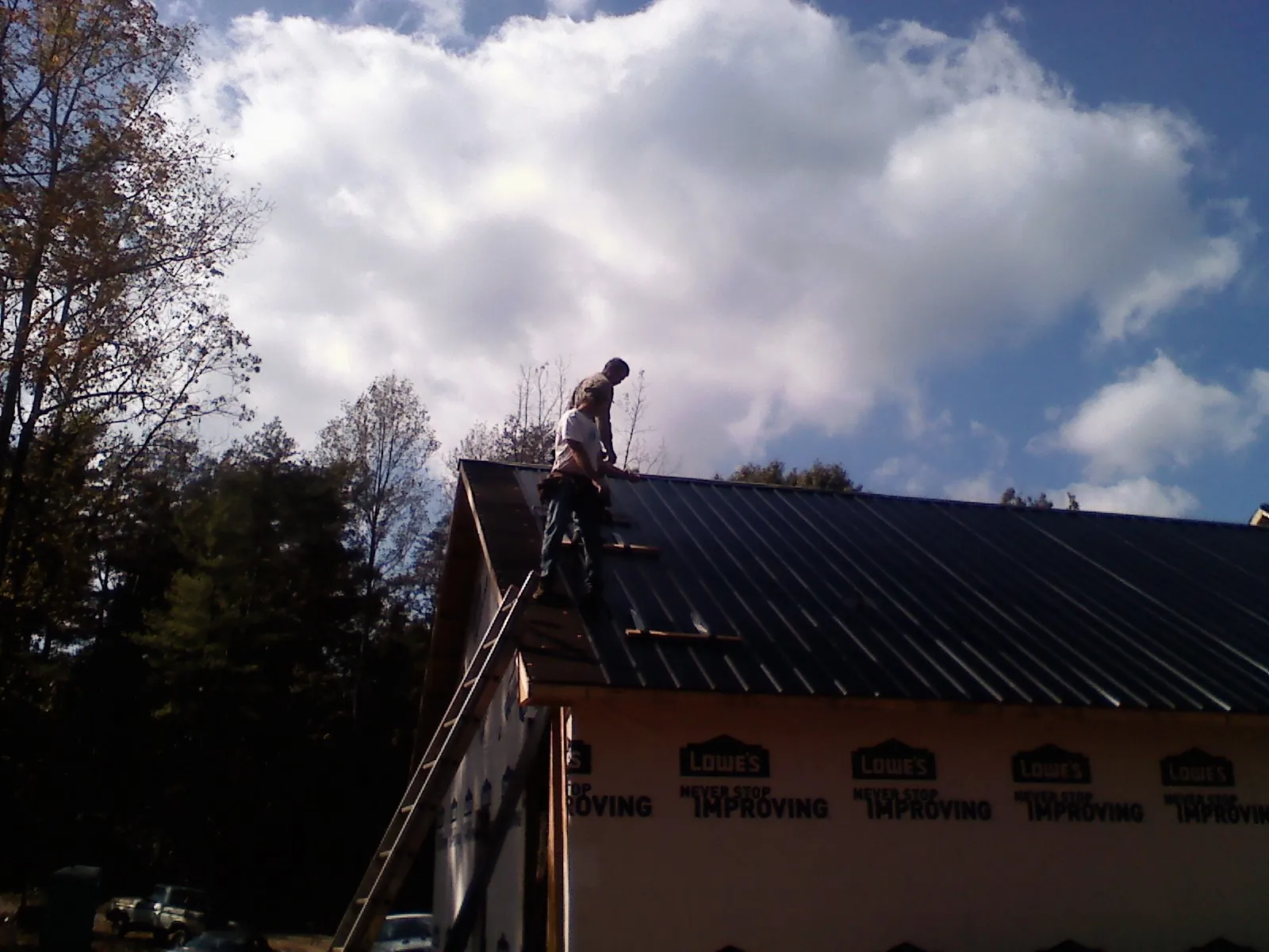Roofer fastening dark metal panels high against a cloudy sky, from a Roof Inspection job in Moundridge