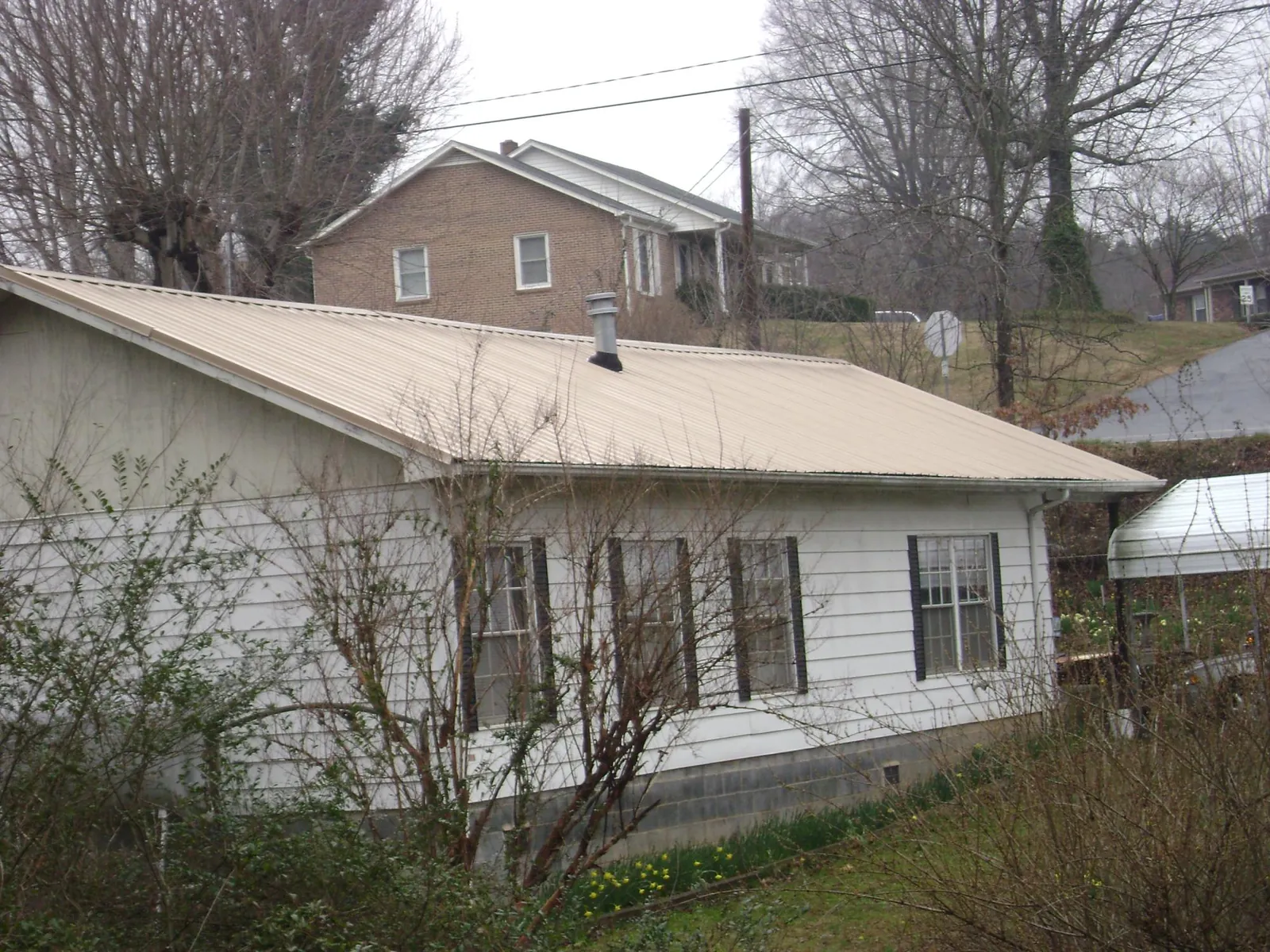 Tan metal roof on a white sided house set into a hillside — Commercial Roofing by Roofing Brothers in Moundridge